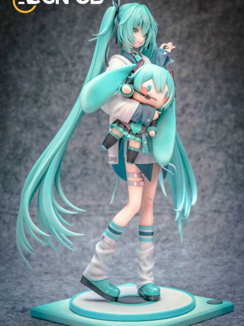 Three-quarter view of Hatsune Miku holding a Miku doll, with sweeping turquoise twin-tails and platform shoes on a teal-and-white base.
