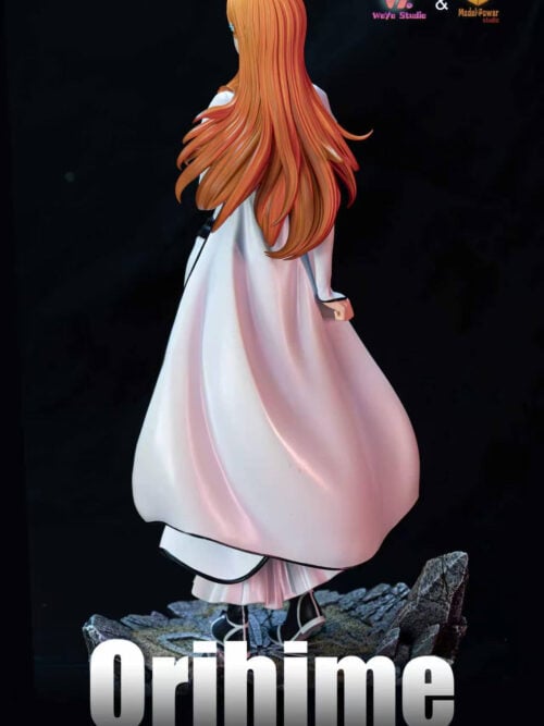 Rear view of Inoue Orihime showing long orange hair, flowing white outfit panels with black edging and the rocky base.