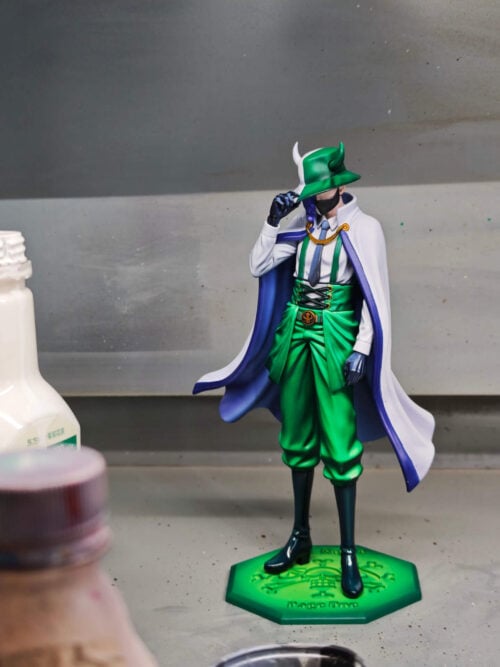 Page One figure touching his horned green hat, wearing a white cape and green trousers on a green octagonal base.