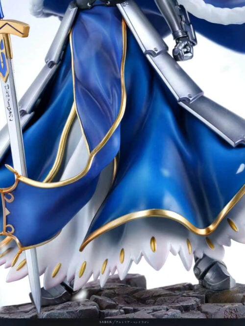 Detail of Altria Pendragon's gold-edged blue skirt, layered silver armor, sword blade and armored boots above broken stonework.