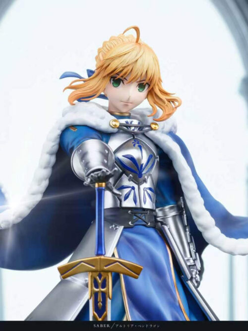 Altria Pendragon's upper body, white-trimmed blue cloak and gold-colored sword guard shown against an arched architectural backdrop.
