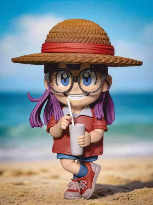 Full view of Arale with a red-banded straw hat, round glasses, cup and crossed-leg pose against a beach backdrop.