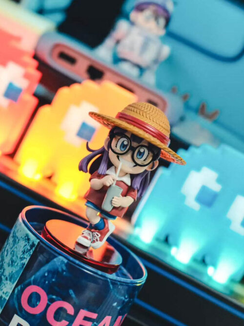Tilted front view of Arale with a textured straw hat, purple hair and cup, standing on a round red base.
