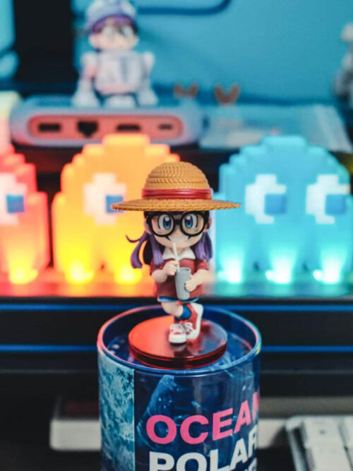 Front view of Arale on a round red base atop a blue cylindrical prop, with colorful arcade-style lights behind her.