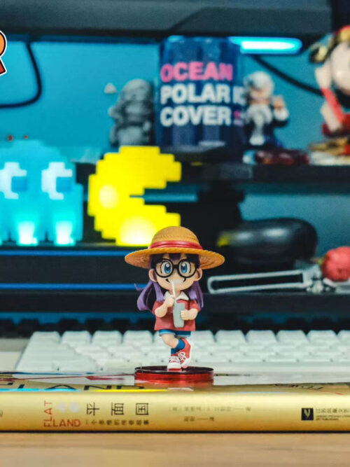 Wide desk view of Arale on her red display base atop a book, in front of a white keyboard and colorful lights.
