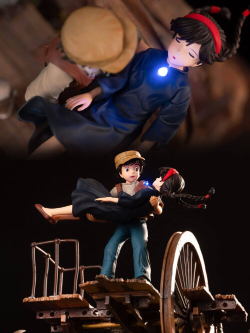 Two-view collage of Sheeta's glowing blue pendant and Pazu holding her above the mine platform beside a large wheel.