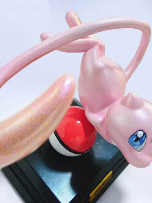 Elevated angled view of Mew above a Poké Ball and dark base, with its broad pink tail sweeping across the foreground.