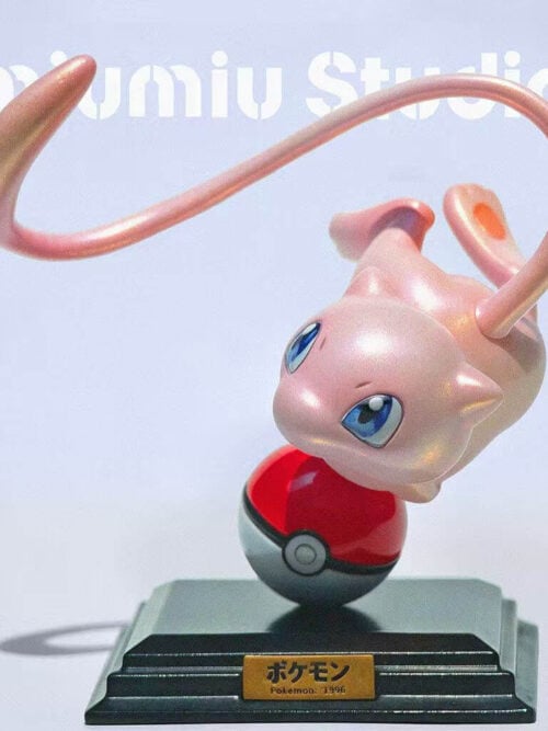 Pink Mew curling headfirst above a Poké Ball, with a looping tail and a dark stepped base with a gold-colored plaque.