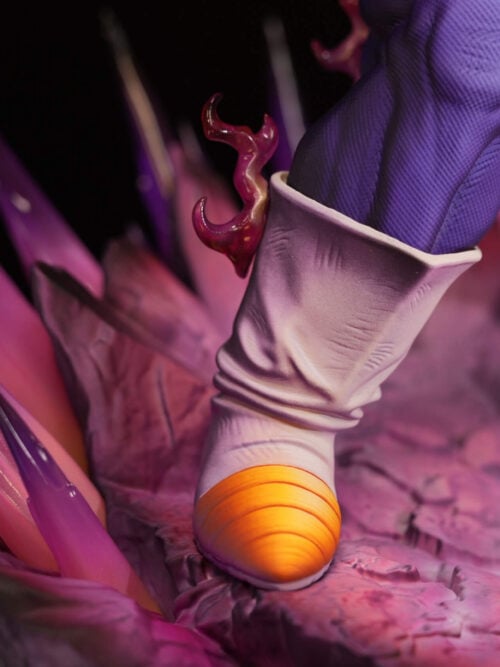 Close-up of Vegeta's white boot with a yellow toe beside pointed pink-purple energy effects and fractured rock textures.