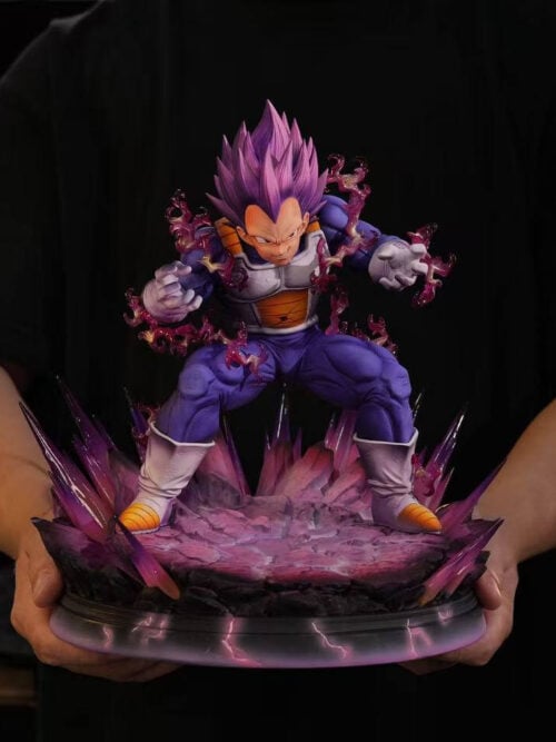 A person holds the complete Ultra Ego Vegeta statue by its base, showing the figure and surrounding purple energy effects.
