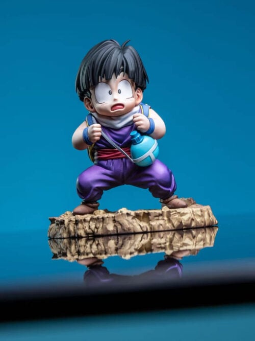 Young Son Gohan prototype gripping backpack straps, with a turquoise canteen and rocky base reflected on a glossy surface.