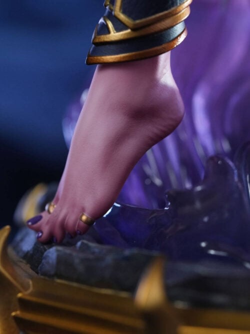 Detail of Xal'atath's bare foot with purple-painted toenails and gold toe rings beside purple effects and the rocky base.