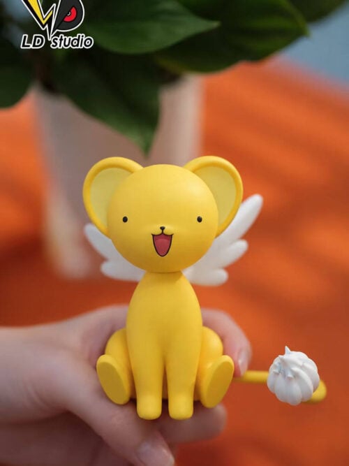 Front view of LD Studio's Kero figure held in a hand, showing an open smile, white wings and a curved yellow tail with a white tuft.