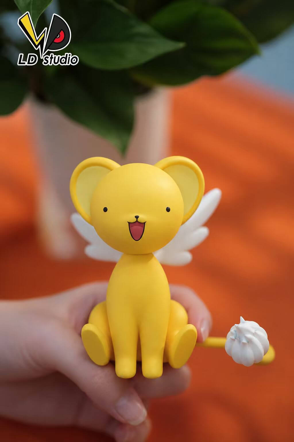 LD Studio Kero — Front View Held in Hand Front view of LD Studio's Kero figure held in a hand, showing an open smile, white wings and a curved yellow tail with a white tuft.