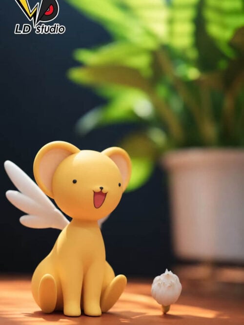 LD Studio's yellow Kero figure seated on a sunlit tabletop, with rounded ears, an open smile, white wings and a white tail tuft.