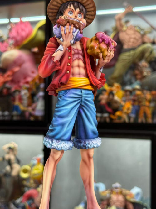 Full view of Luffy holding two icing-covered cakes, wearing a straw hat, red jacket, blue shorts and sandals.