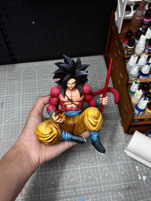 Son Goku Belt Version figure held over a cutting mat, showing the full seated pose, upright red staff and curling tail.
