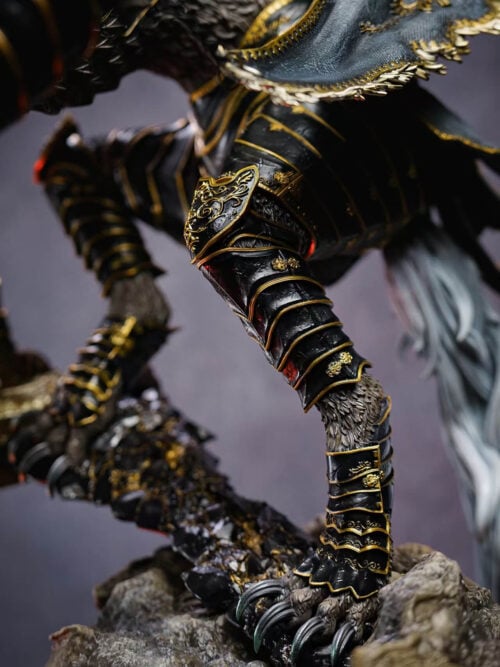 Close-up of Maliketh's layered black-and-gold leg armor and clawed foot beside the sword and broken masonry.