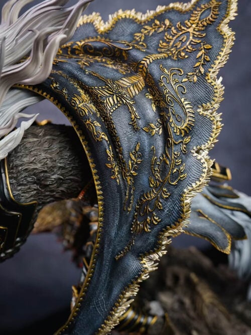 Close-up of Maliketh's dark textured cape with raised gold-colored motifs and a fringed edge beside white hair.