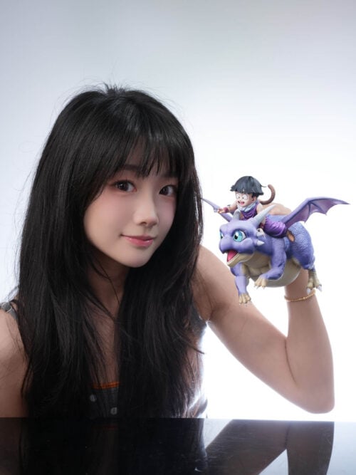 A person holds Son Gohan riding Icarus beside their face, with the scenic base absent from the photograph.