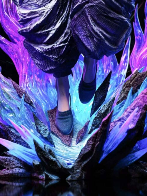 Close-up of the display base showing Satoru Gojo's wide white trousers and dark slip-on shoes suspended above jagged rock shards and illuminated blue-and-purple energy plumes.