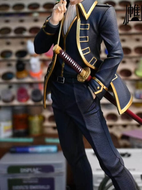 Mid-section close-up of the Toushirou Hijikata statue showing his left hand tucked into his trouser pocket beside the diamond-wrapped hilt and red scabbard of his katana