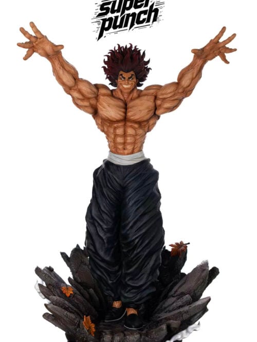SuperPunch Studio Yujiro Hanma statue from Baki the Grappler in full front view against a white background, sculpted shirtless with raised arms, black trousers, and a jagged dark rock base with autumn leaves.
