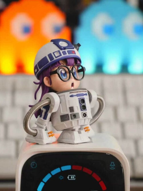 Close-up of TOR Studio Arale Series Vol. 28 WCF-scale figure showing Arale's wide blue eyes behind round black glasses, open mouth, blue-and-white domed droid helmet, paneled cylindrical torso, and coiled metal hose arms.