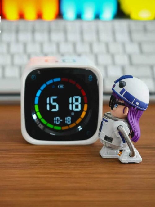 Left side profile of TOR Studio Arale Series Vol. 28 WCF-scale figure on a wooden desk facing a digital clock, showing her long purple hair extending from beneath the domed helmet down the back of the cylindrical droid body.