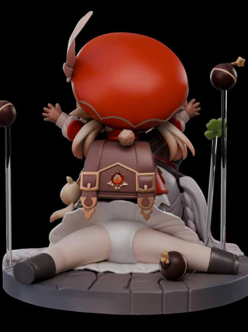 Rear view of the XingYu Studio Klee and Sparxie chibi statue showing Klee's red hat and brown backpack with a Pyro emblem above Sparxie's legs and the round stone base.