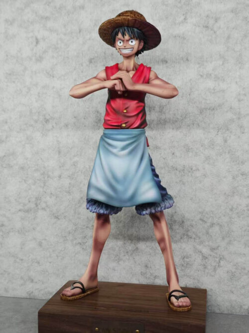 Angled view of Monkey D. Luffy with hands together, a light blue waist apron over blue shorts, and sandals on a wooden base.