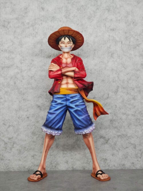 Luffy shown from the front with closed eyes and crossed arms, standing wide-legged in sandals beneath a textured straw hat.