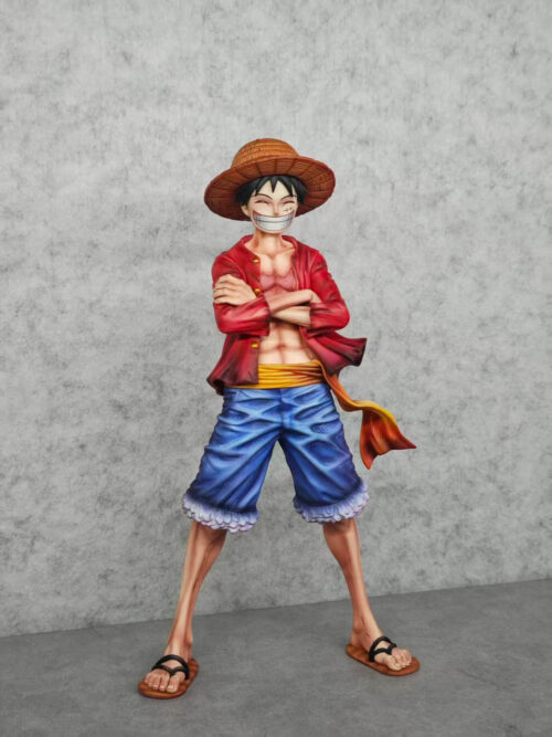 Slightly angled full view of Luffy with crossed arms, a flared red jacket and a yellow sash extending beside his blue shorts.