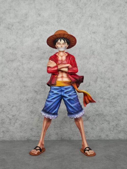 Full-length front view of Luffy against a gray backdrop, grinning with arms crossed and sandaled feet spread apart.