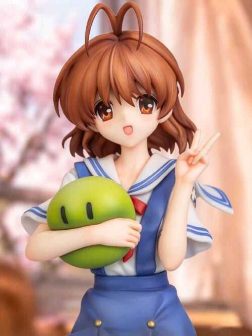 Close-up of Nagisa Furukawa's smiling face, raised peace sign, blue-trimmed sailor collar and green mascot held against her chest.