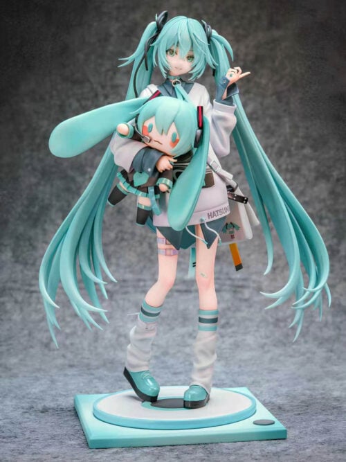 Full front view of Hatsune Miku holding a large Miku doll, with turquoise twin-tails and white leg warmers on a teal-and-white base.