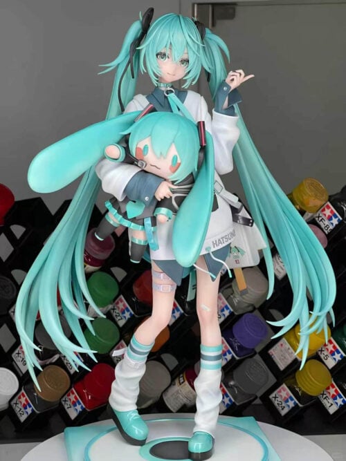 Front view of Hatsune Miku holding a Miku doll in front of paint racks, showing her raised hand, shoulder bag and long turquoise twin-tails.