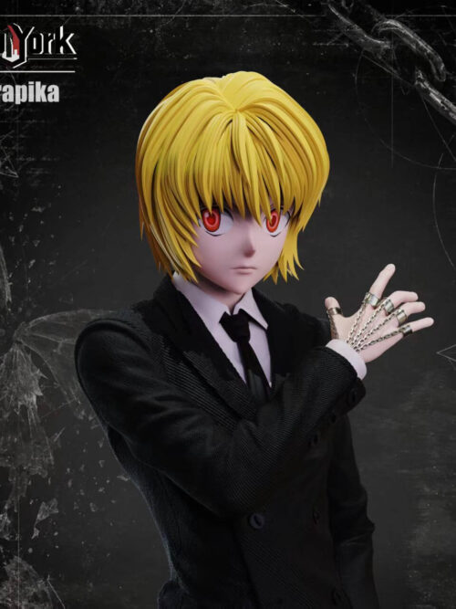 Close-up of Kurapika's blond hair, red eyes and raised hand with finger rings and chains above the lapels of his black suit.