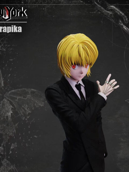 Three-quarter upper-body view of Kurapika in a textured black suit, showing his blond fringe, red eyes and chains across his raised hand.