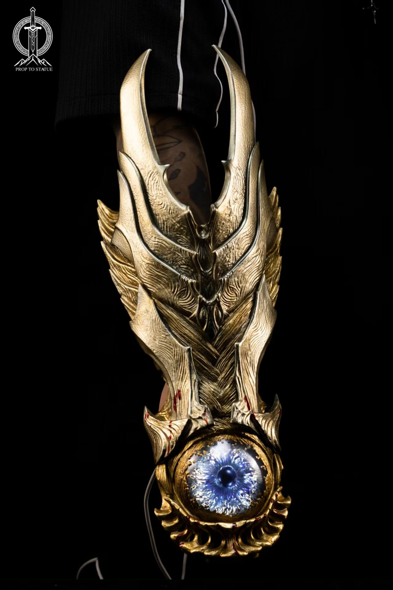 Onimusha Oni Gauntlet - Full Vertical View Full vertical view of the Oni Gauntlet on an arm, showing pointed gold-toned armor, a glowing blue eye-like centerpiece and red blood markings.