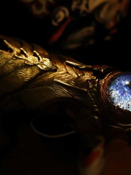 Low-angle close-up of the Oni Gauntlet, with layered gold-toned armor extending behind the glowing blue eye-like centerpiece.