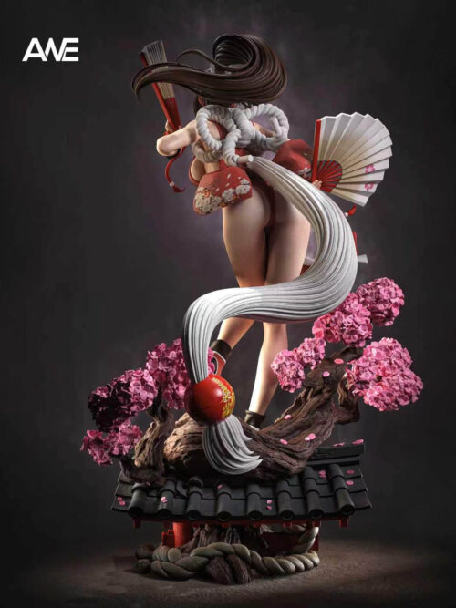 Rear view of Mai Shiranui showing looped white rope, a patterned red bow and a long white tassel above pink blossoms and roof tiles.