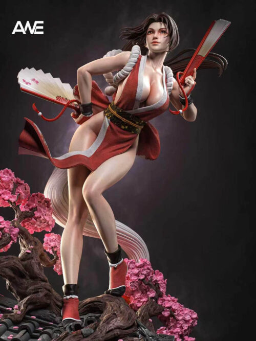 Low-angle detail of Mai Shiranui with two red-and-white fans, white shoulder ropes and a patterned sash, with pink blossoms below.