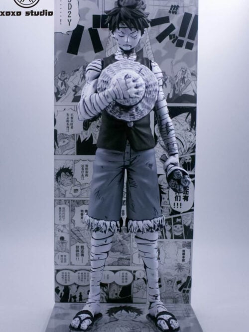 Full front view of black-and-white Luffy holding his straw hat and a bouquet, with a manga-panel backdrop and illustrated base.