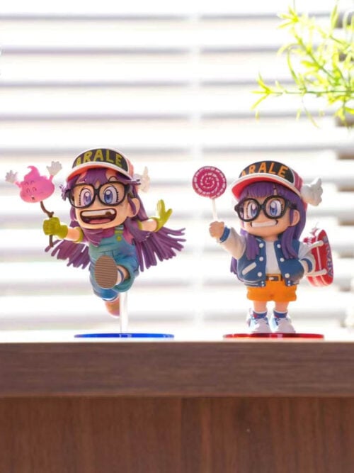 Lollipop Arale on a red base beside a separate running Arale figure on a blue base in a windowsill display.