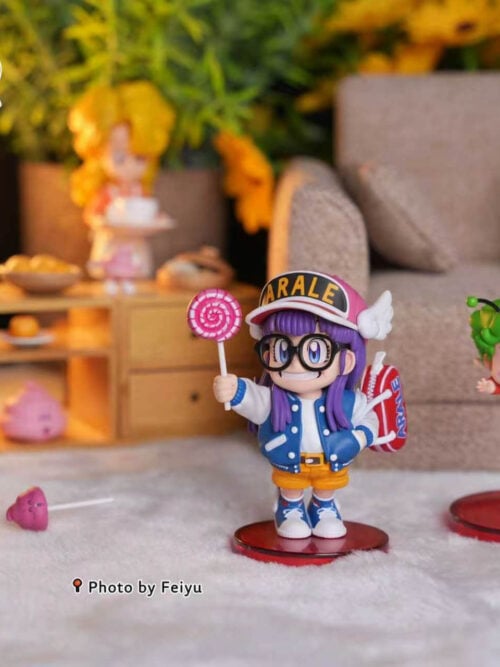 Arale holding a pink lollipop on a red base, with a loose pink poop accessory and other figures in a miniature room.