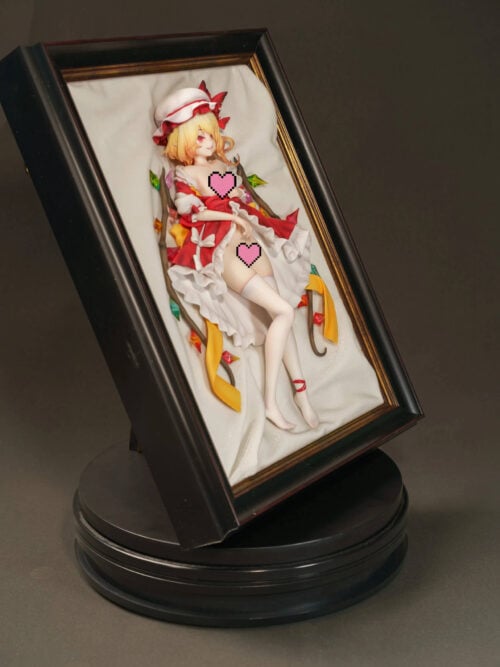 Censored angled photo of Flandre Scarlet in a deep black-and-gold frame, with white drapery, colorful wing ornaments and yellow ribbons.