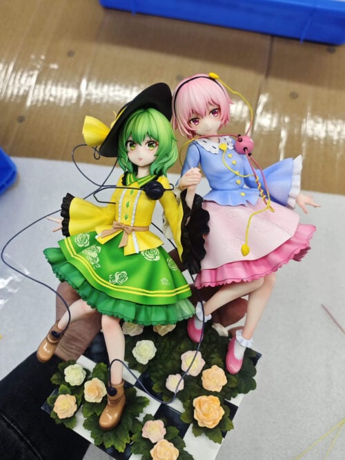 Koishi Komeiji and Satori Komeiji holding hands in yellow-and-green and blue-and-pink outfits above a rose-covered checkerboard base.