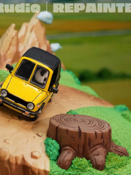 Yellow car on a winding dirt path beside a tree stump, grassy terrain and miniature mountain peaks, shown without Goku.