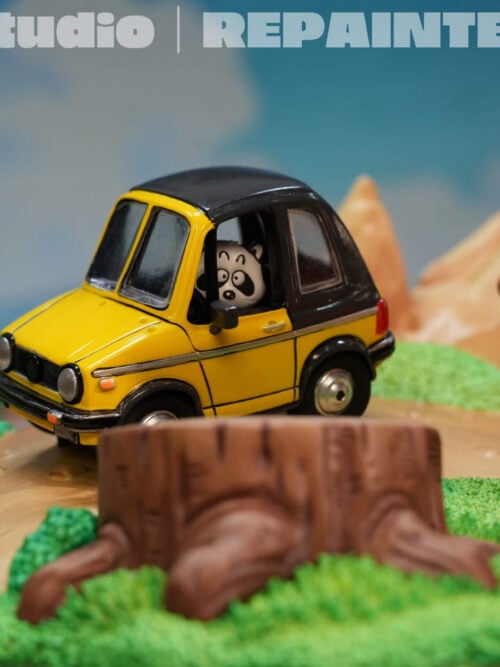 Close-up of the yellow car with a black roof and panda-like driver, beside Goku's orange outfit and staff carrier.